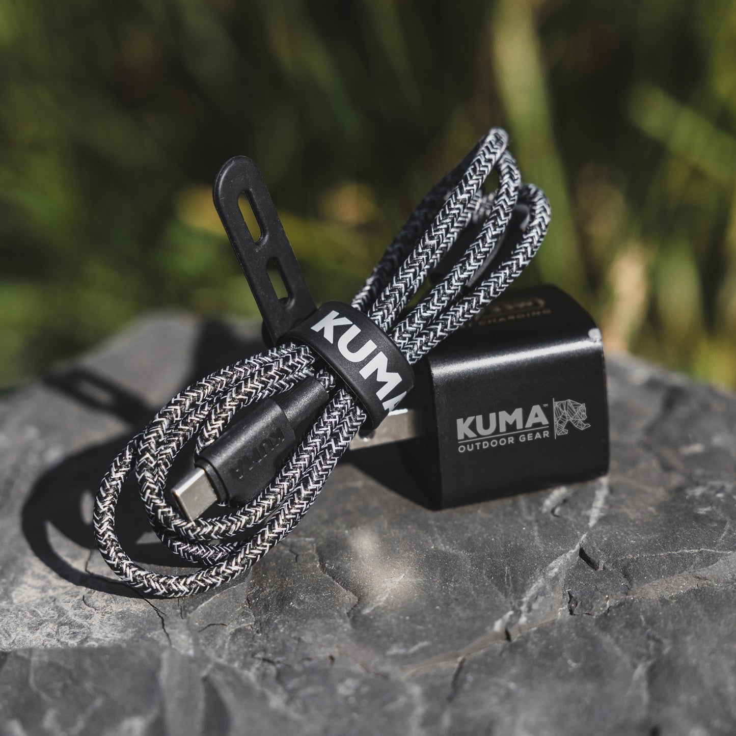 Compact KUMA USB charger for RV and travel use with braided cord on a stone surface