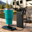 KUMA Portable USB-C Power Bank and Kona Tumbler displayed on a campsite picnic table beside an RV.