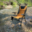 Foldable chair with brown seat and black backrest on a rocky riverbank.
