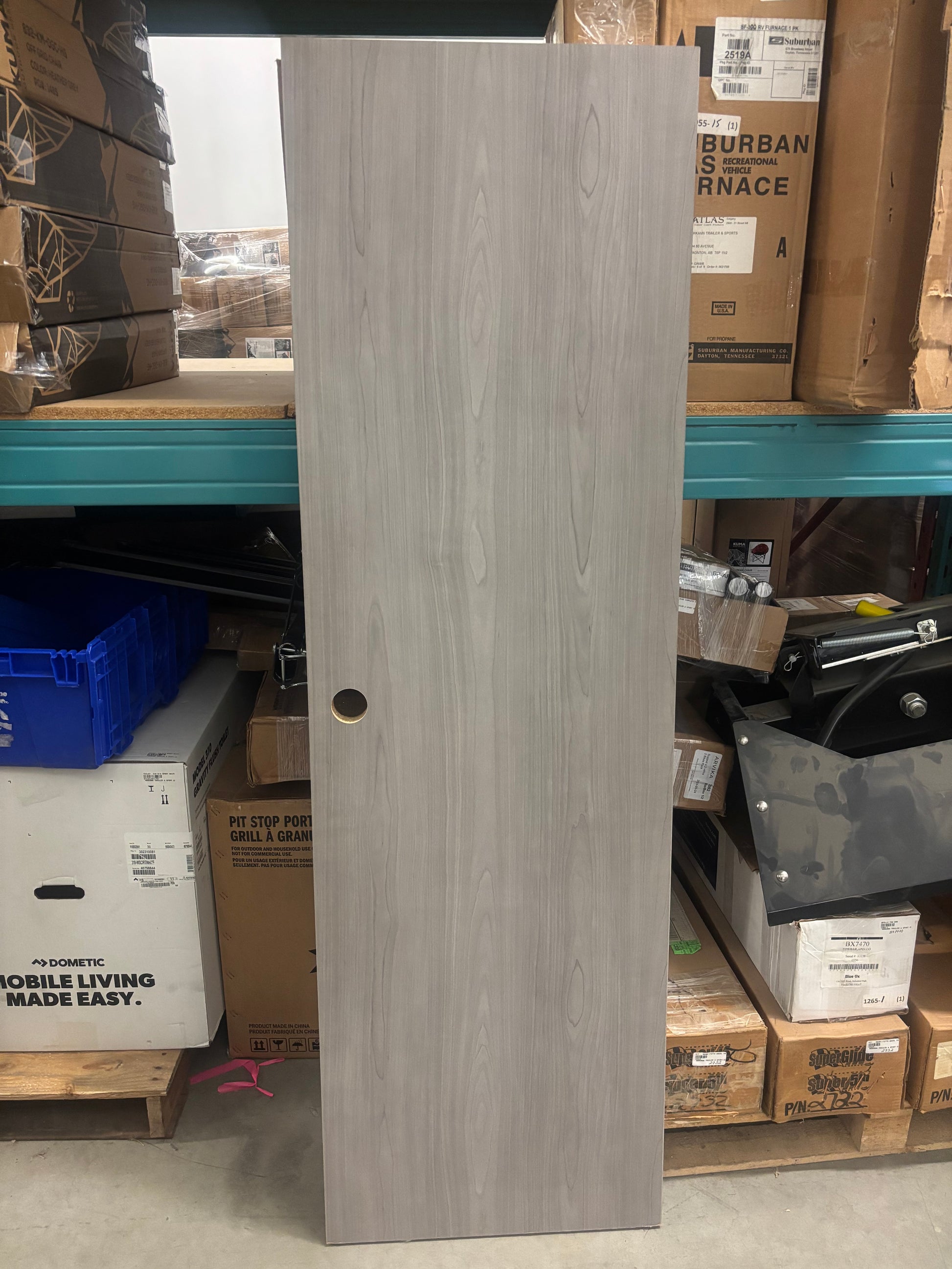 A silverton maple cabinet door standing upright on a shelf with various items in the background.
