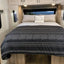 A bed with a black and gray boho patterned duvet cover and pillowcases, set in a camper or RV with a window and decorative pillow.