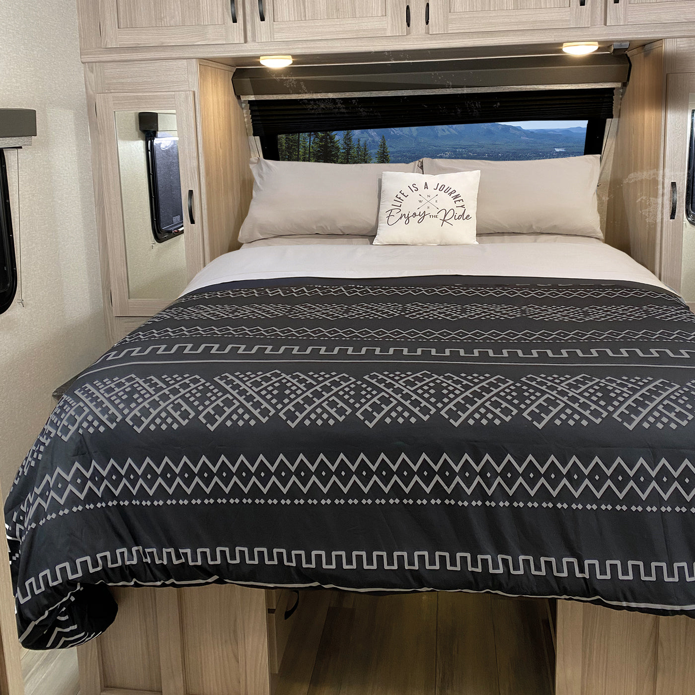 A bed with a black and gray boho patterned duvet cover and pillowcases, set in a camper or RV with a window and decorative pillow.