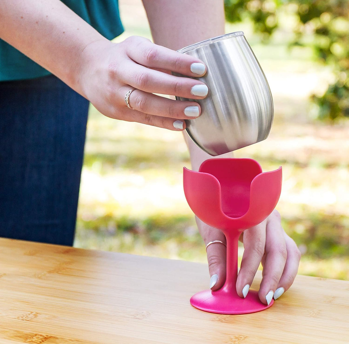 Person holding a silver cup with a pink silicone cup holder on a wooden surface.