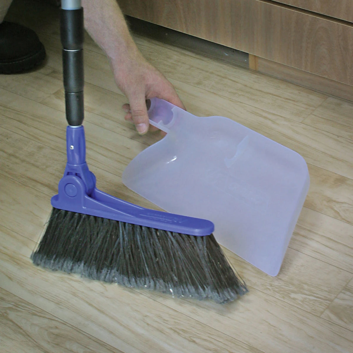 Person using a broom and dustpan on a wooden floor
