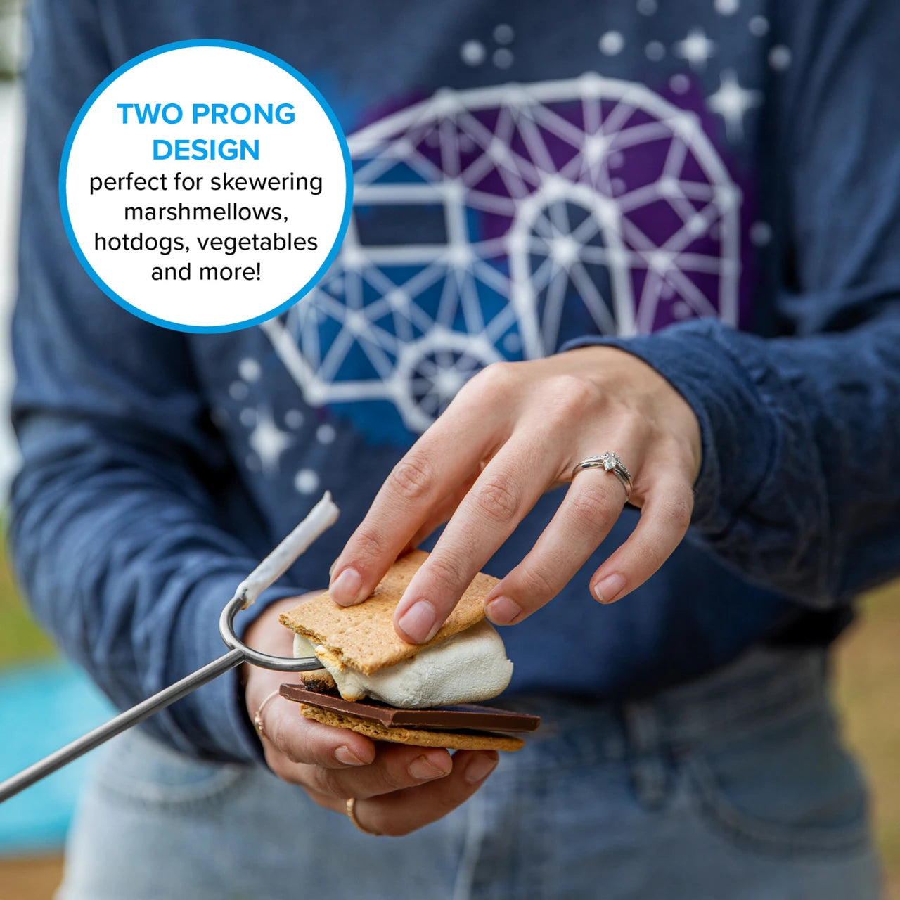 Person holding a s'more with skewer, wearing a blue shirt with a geometric design.