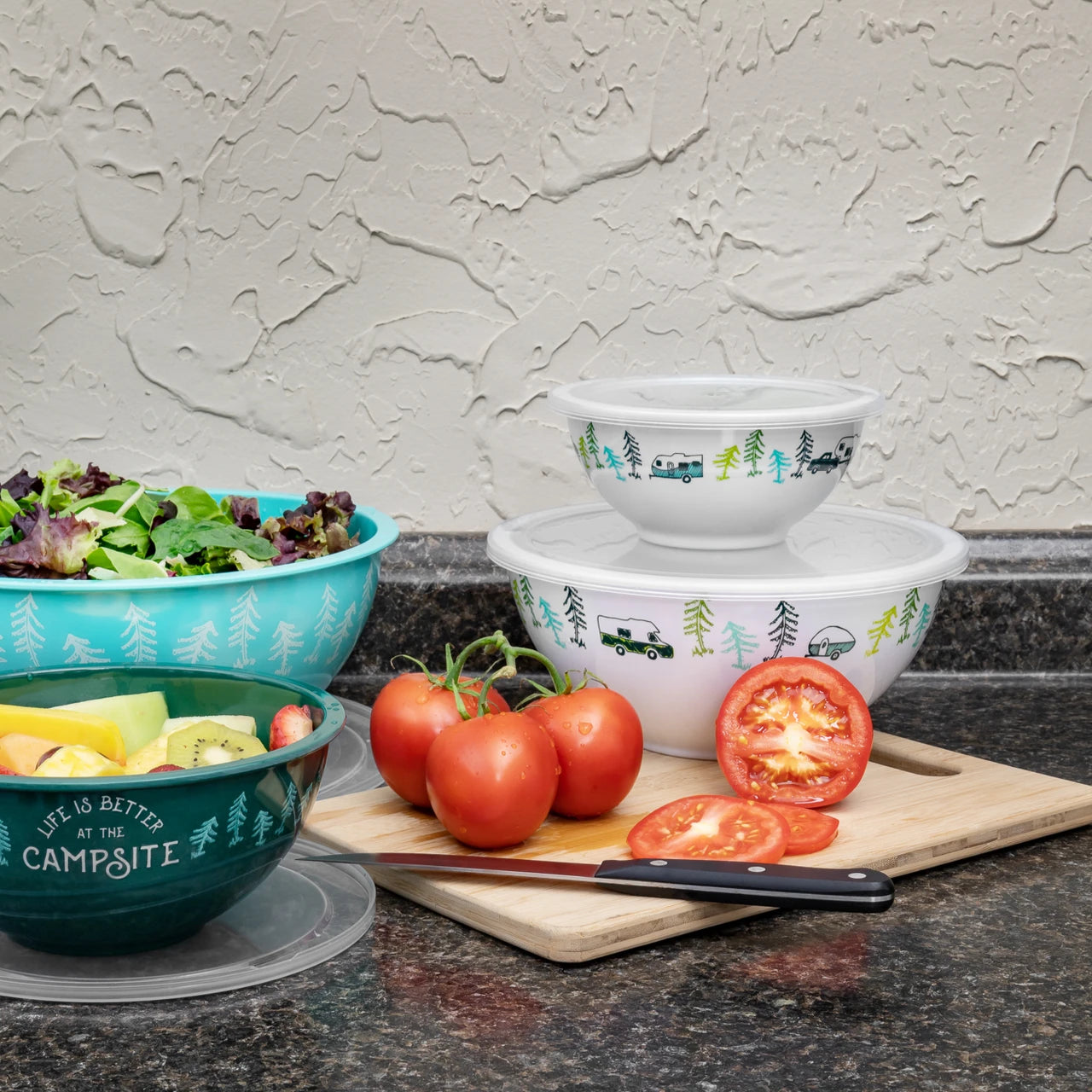 Stack of nesting bowls with nature-themed design on a kitchen counter with tomatoes and salad.