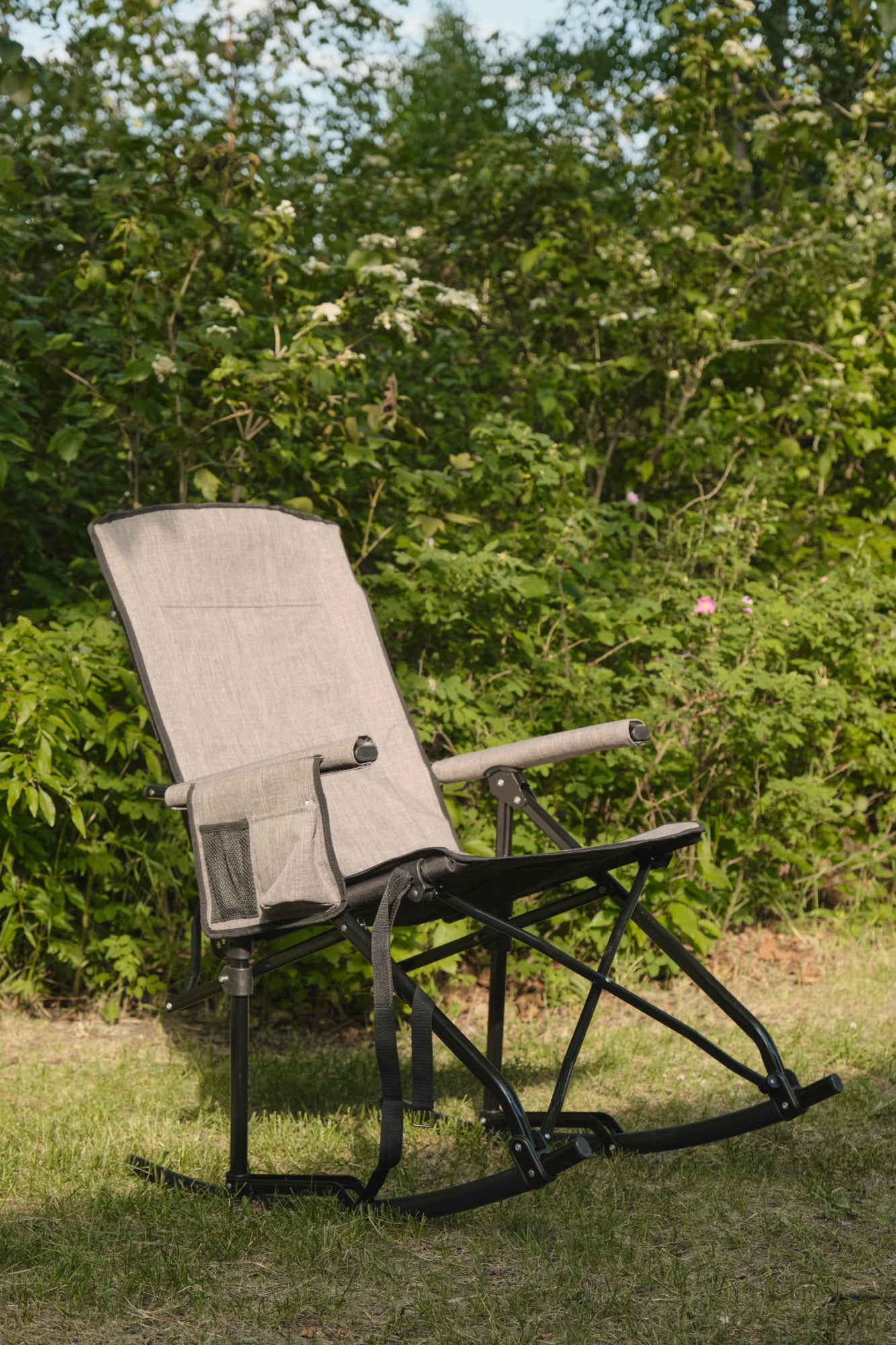 Foldable rocking chair on grass with greenery in the background
