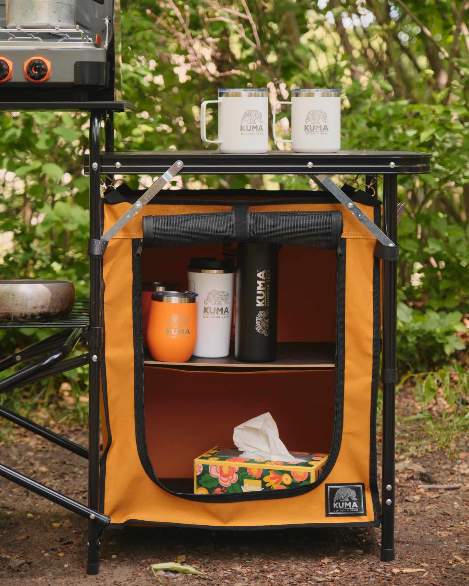 Outdoor setup with a portable storage unit, camping stove, and Kuma branded items.