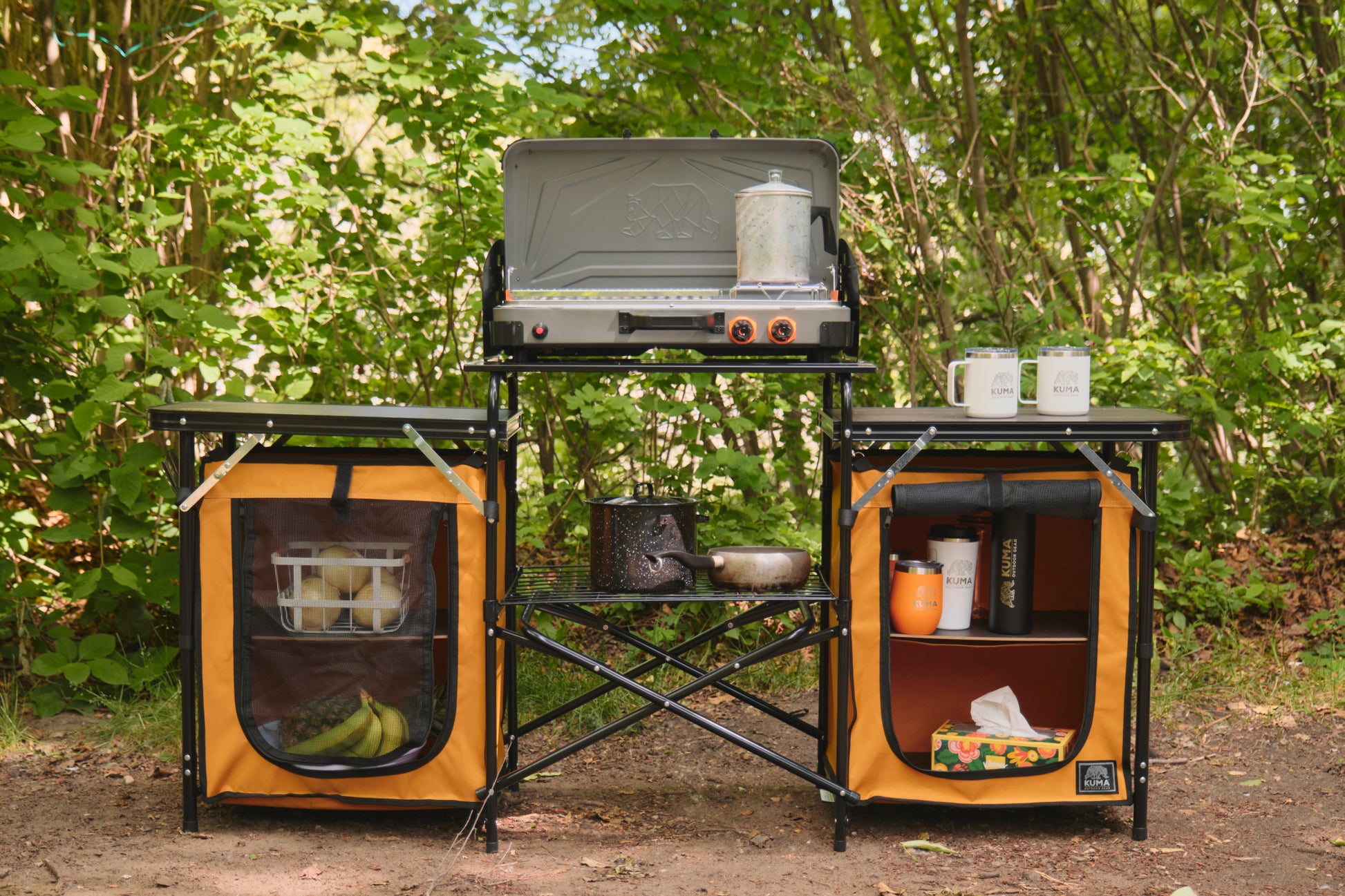 Outdoor camping stove with cabinets and supplies in a forest setting
