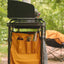 Camping stove with orange pot holder and accessories in a forest setting