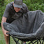 Person setting up a gray fleece blanket on a camping chair outdoors.