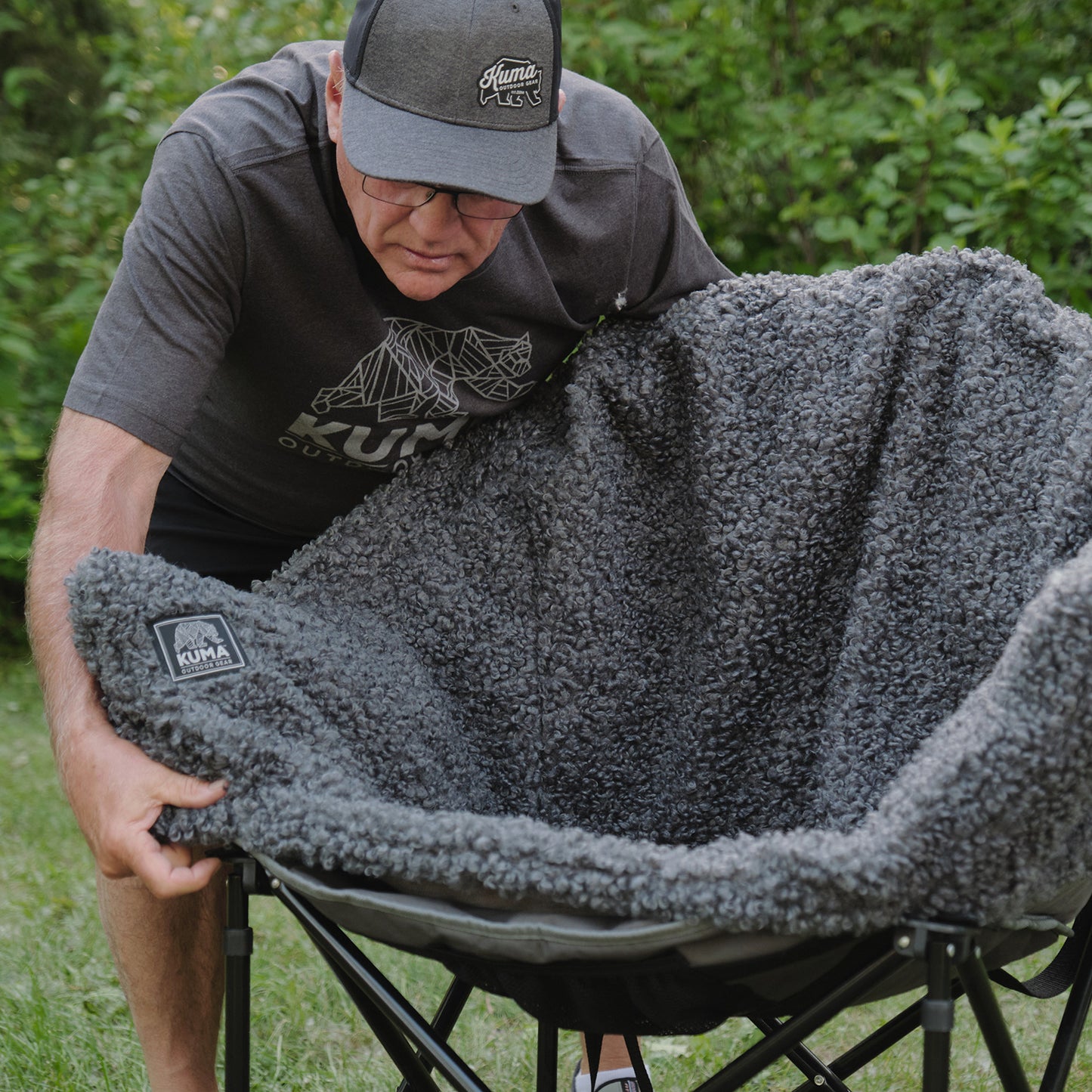 Person setting up a gray fleece blanket on a camping chair outdoors.