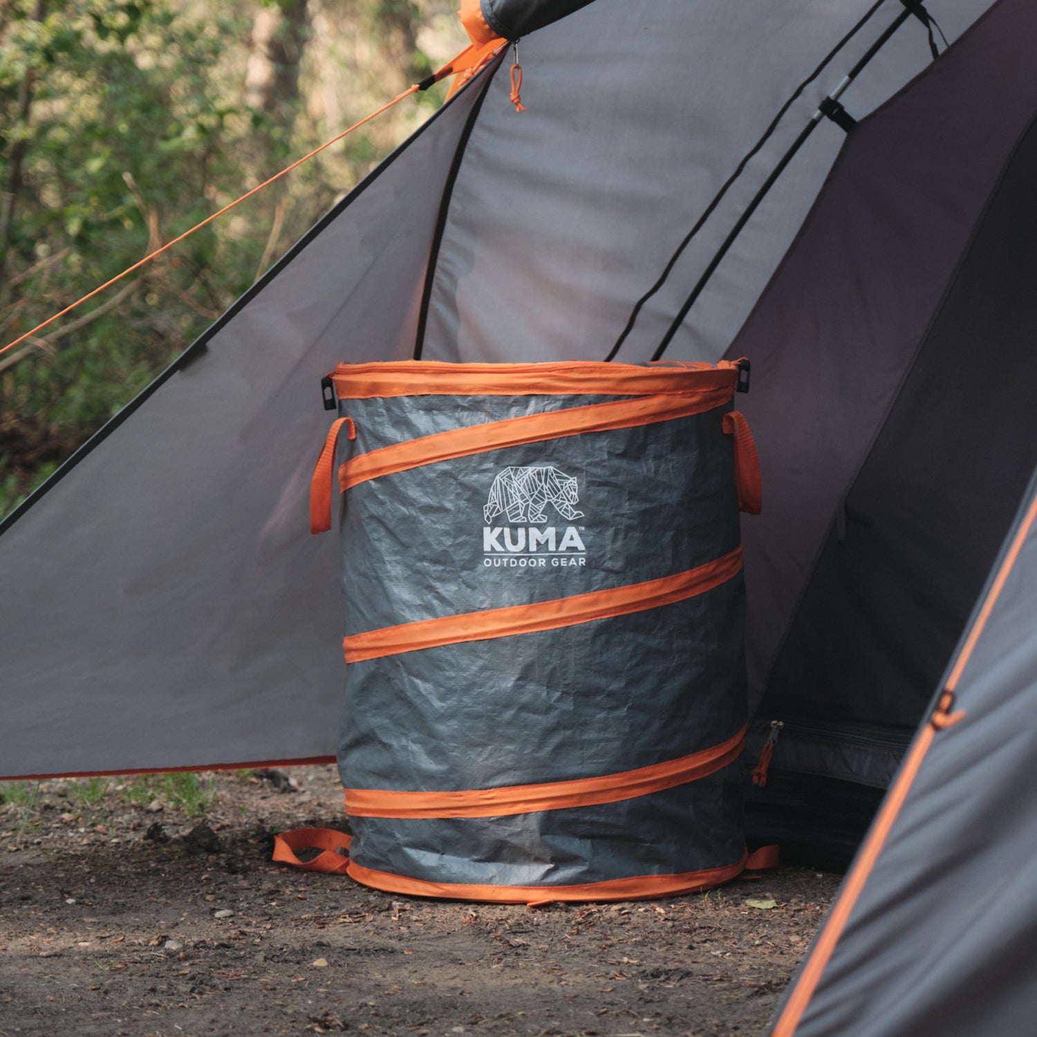 Kuma outdoor gear trash can next to a tent in a forest setting