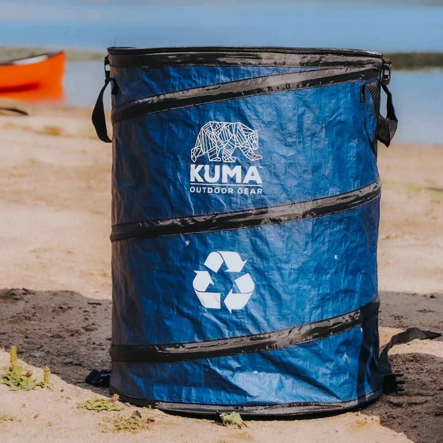 Blue recycling bin with Kuma Outdoor Gear logo on a beach
