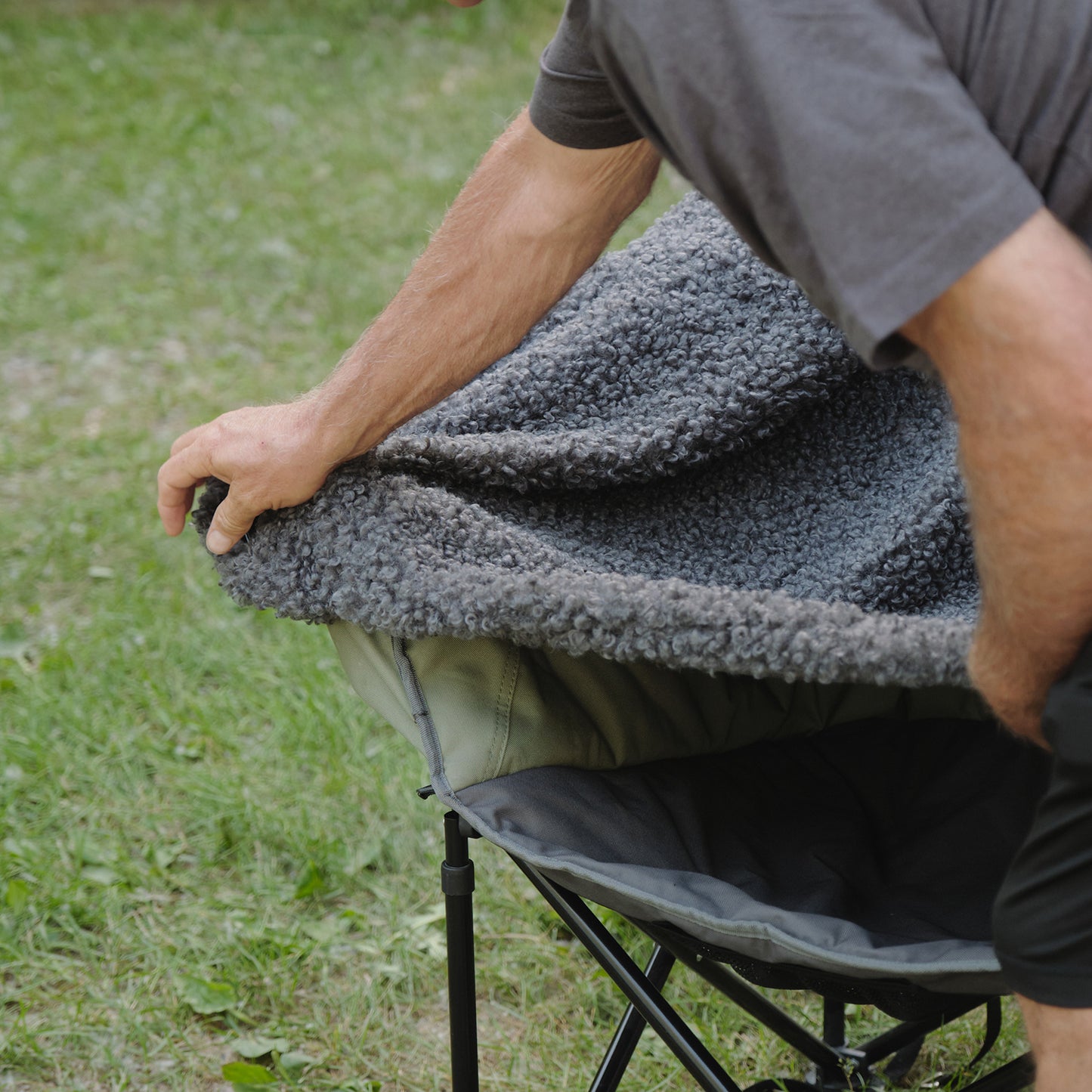 Person adjusting a gray teddy bear fabric on a camping chair outdoors.