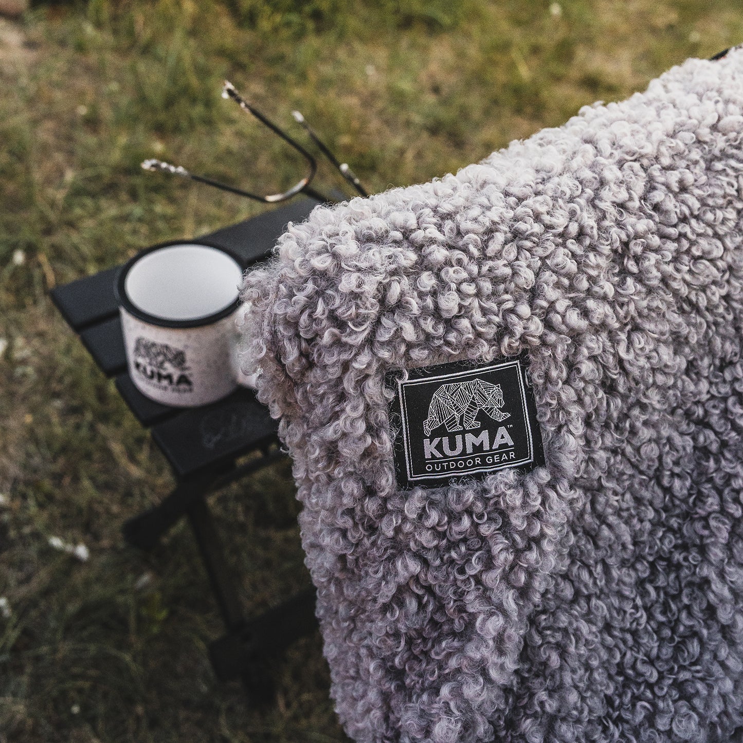 Gray sherpa blanket with Kuma Outdoor Gear logo on a grassy background
