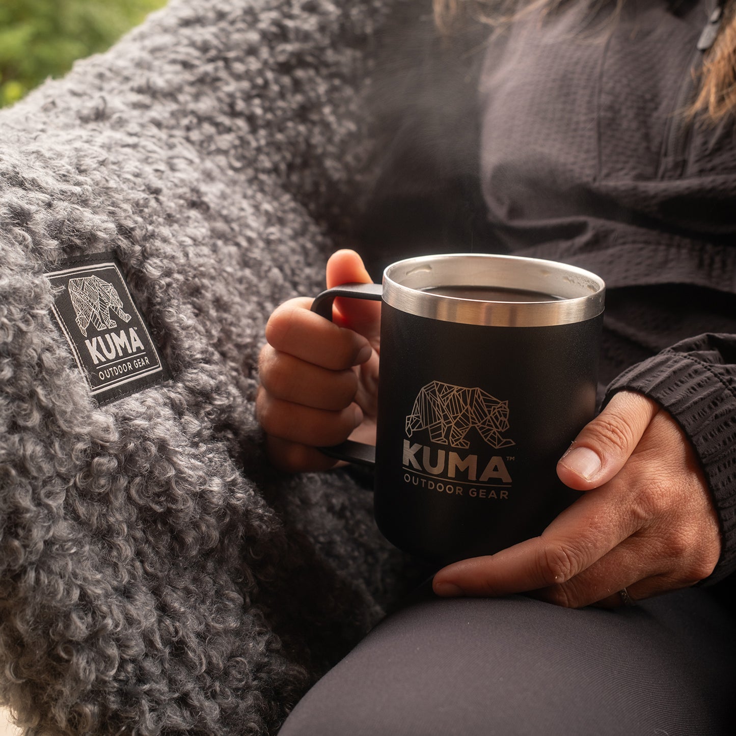Person holding a Kuma Outdoor Gear mug with a blurred natural background